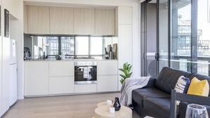 A modern kitchen with white cabinets, a stainless steel oven, and a large window. - Docklands high level 1 Bedroom Apartment with pool by KozyGuru (Docklands)