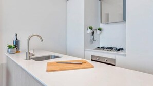 Une cuisine moderne dotée d’un plan de travail blanc, d’un évier en acier inoxydable et d’une cuisinière à gaz intégrée.
