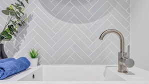 Une salle de bain moderne avec un lavabo blanc, un robinet incurvé, une plante en pot et une serviette bleue.