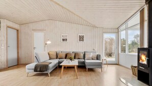 Una sala de estar moderna con techo de madera, un sofá seccional gris, una mesa de centro de vidrio y un estufa de leña.