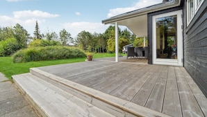 Una terraza de madera que conduce a un porche cubierto con mobiliario exterior.
