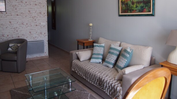 Ein Wohnzimmer mit grauem Sofa, gemusterten Kissen, einem Glastisch und einem gerahmten Gemälde an der Wand.