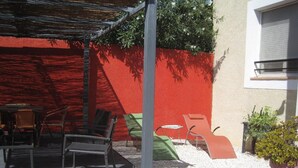 Eine Terrasse im Freien mit Metallstühlen, einem Tisch, einer roten Wand und einem Blumentopf.