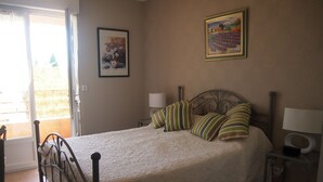 Ein Schlafzimmer mit einem Bett, Kissen, einem Nachttisch, einer Lampe und zwei gerahmten Kunstwerken an der Wand.