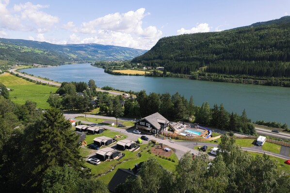 Una propiedad junto al lago con piscina, varias cabañas y un edificio grande con techo inclinado.