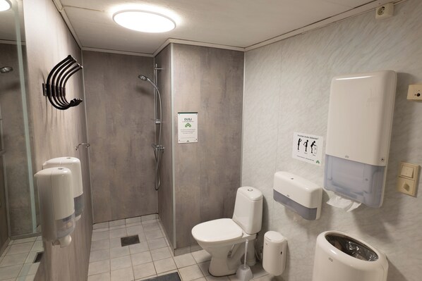 A modern bathroom with a shower, toilet, hand dryer, and paper towel dispenser.