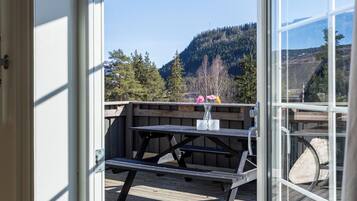 A wooden deck with a picnic table and a vase of flowers, overlooking a forested hillside.