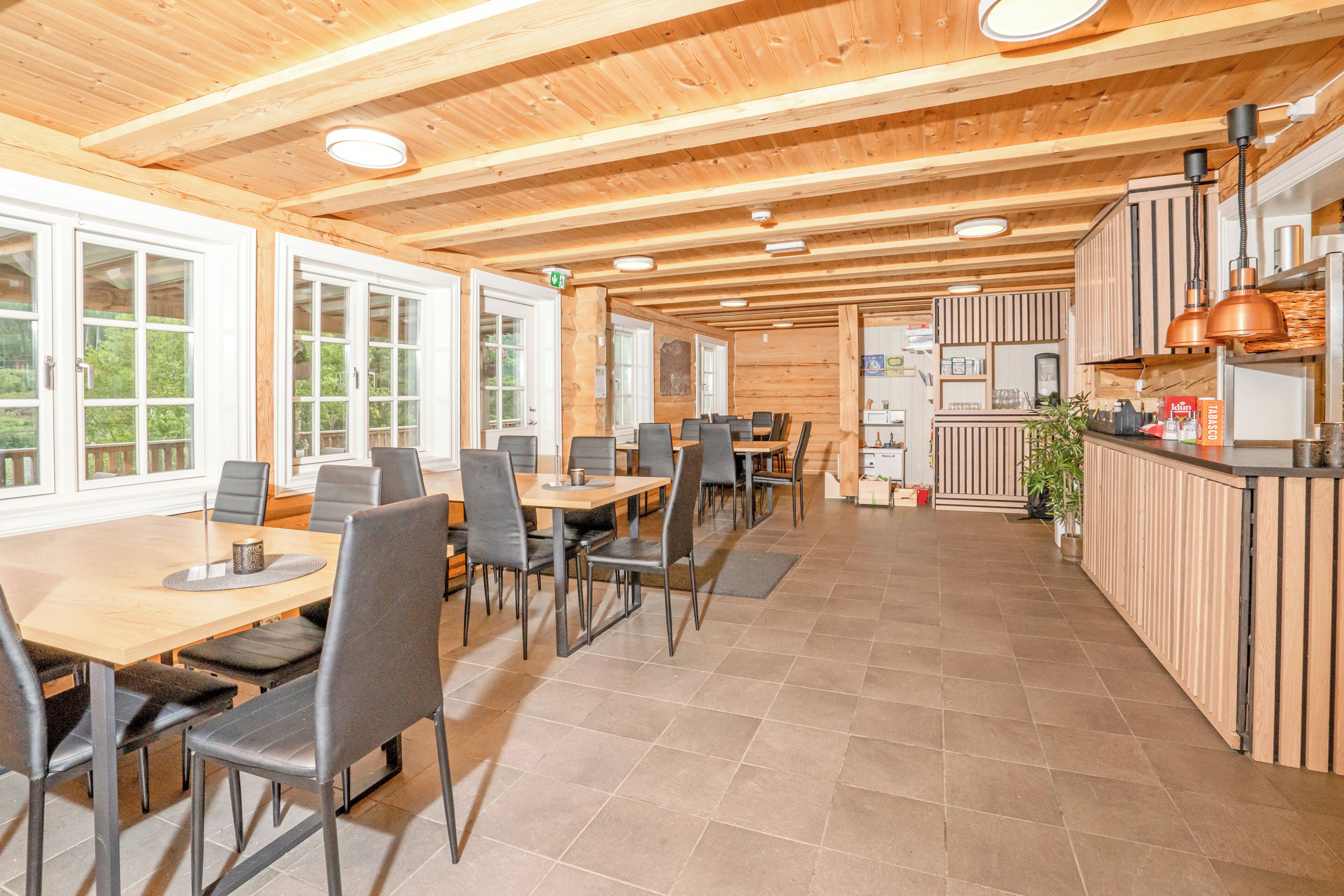 A wooden interior with a dining area, kitchen, and large windows.