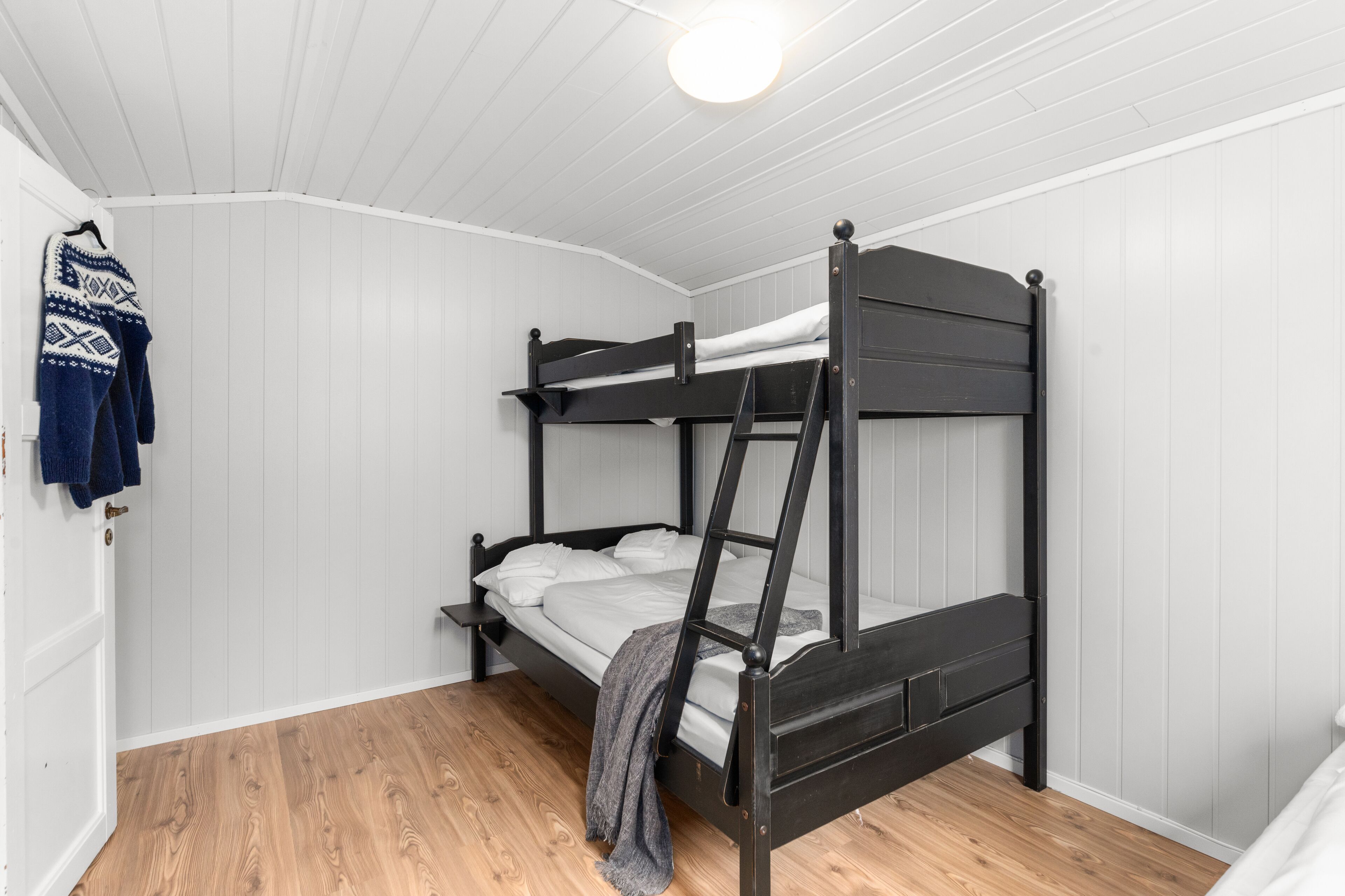 A bunk bed in a room with white paneled walls and wooden flooring.