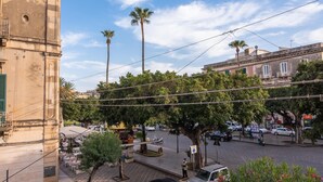 Une vue de rue avec un immeuble, des voitures et un balcon doté d’une balustrade.