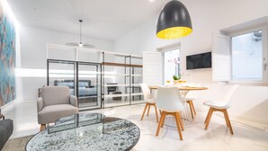 Un salon moderne avec une table en verre, des chaises blanches, un canapé et une grande fenêtre.
