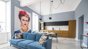 Un salon moderne avec un canapé bleu, un grand tableau et une cuisine en arrière-plan.