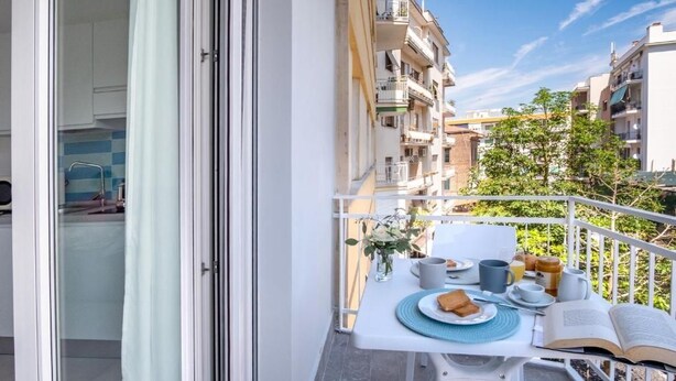 Parvekkeella on aamiasta varten katettu pöytä, sieltä avautuu näkymä kaupunkiin, ja ovi johtaa huoneeseen.