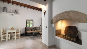 Ein gemütliches Interieur mit Kamin aus Stein, einem Essbereich mit Tisch und Stühlen sowie einer Sitzecke mit Kissen.