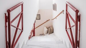 Eine Treppe mit roten Geländern führt zu einer Zwischenebene mit einem Bett und Kissen.
