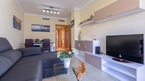 A modern living room with a sofa, a dining area with chairs, a TV, and a decorative plant. - Stunning apartment in Benalmádena with WiFi (Benalmádena)