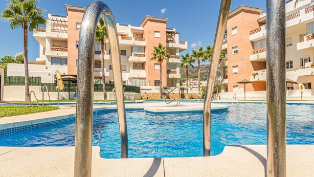 A swimming pool with clear blue water, surrounded by palm trees and a building with balconies. - Stunning apartment in Benalmádena with WiFi (Benalmádena)