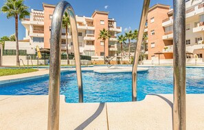 Una piscina con agua azul cristalina, rodeada de palmeras y un edificio con balcones.