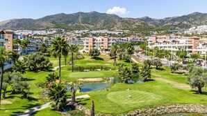 A golf course with a pond, surrounded by palm trees and a residential area with apartment buildings. - Stunning apartment in Benalmádena with WiFi (Benalmádena)