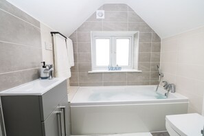 A modern bathroom with a bathtub, a toilet, and a sink. There is a window above the bathtub and a towel rack on the wall.