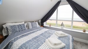 A bedroom with a large bed, a window with curtains, and a view of the beach. - Ocean View (Hayling Island)