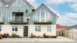 A two-story residential building with a balcony on the upper floor, a front door, and a small garden area with plants. - Ocean View (Hayling Island)