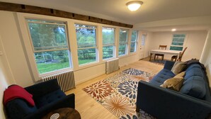 A spacious living room with a blue sofa, a wooden coffee table, and a patterned rug. Large windows provide a view of the outdoors. - Mountain View Farmhouse, pool/hot tub, fire pit, 4 seasons porch, game room (Millerton)