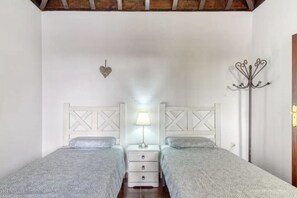 A bedroom with two beds, a nightstand with a lamp, a coat rack, and a heart-shaped decoration on the wall. - Charming Casa Flamenca: Private, Scenic Retreat with Pool and Mountain (Tijarafe)