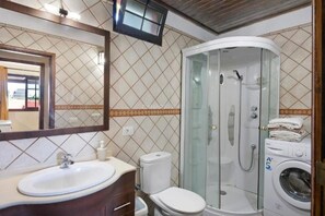 A bathroom with a sink, toilet, glass-enclosed shower, and a washing machine.