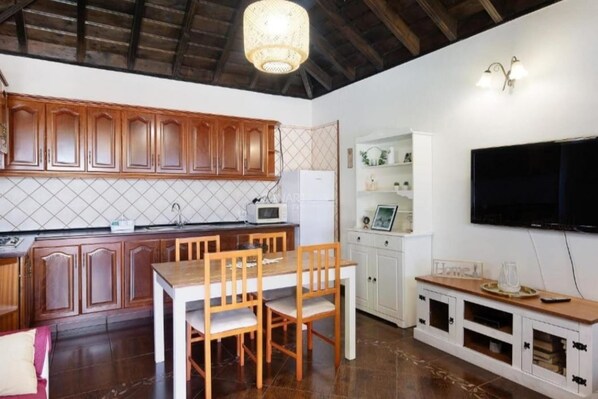 A kitchen with wooden cabinets, a dining table, chairs, a microwave, and a TV mounted on the wall.