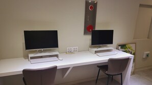 Un espace de bureau moderne comprenant deux ordinateurs de bureau, un bureau blanc, deux chaises et un détecteur d’incendie fixé au mur.