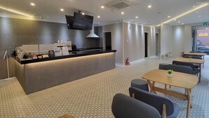 Un hall d’hôtel moderne comprenant un comptoir d’accueil, un espace salon et un grand écran de télévision.