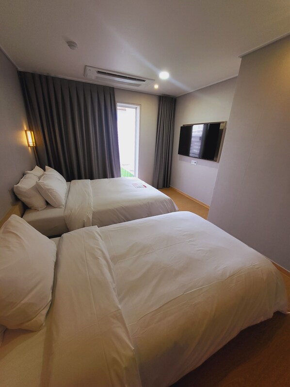 Ein Hotelzimmer mit zwei Betten, einem an der Wand befestigten Flachbildfernseher und einem Fenster mit Vorhängen.