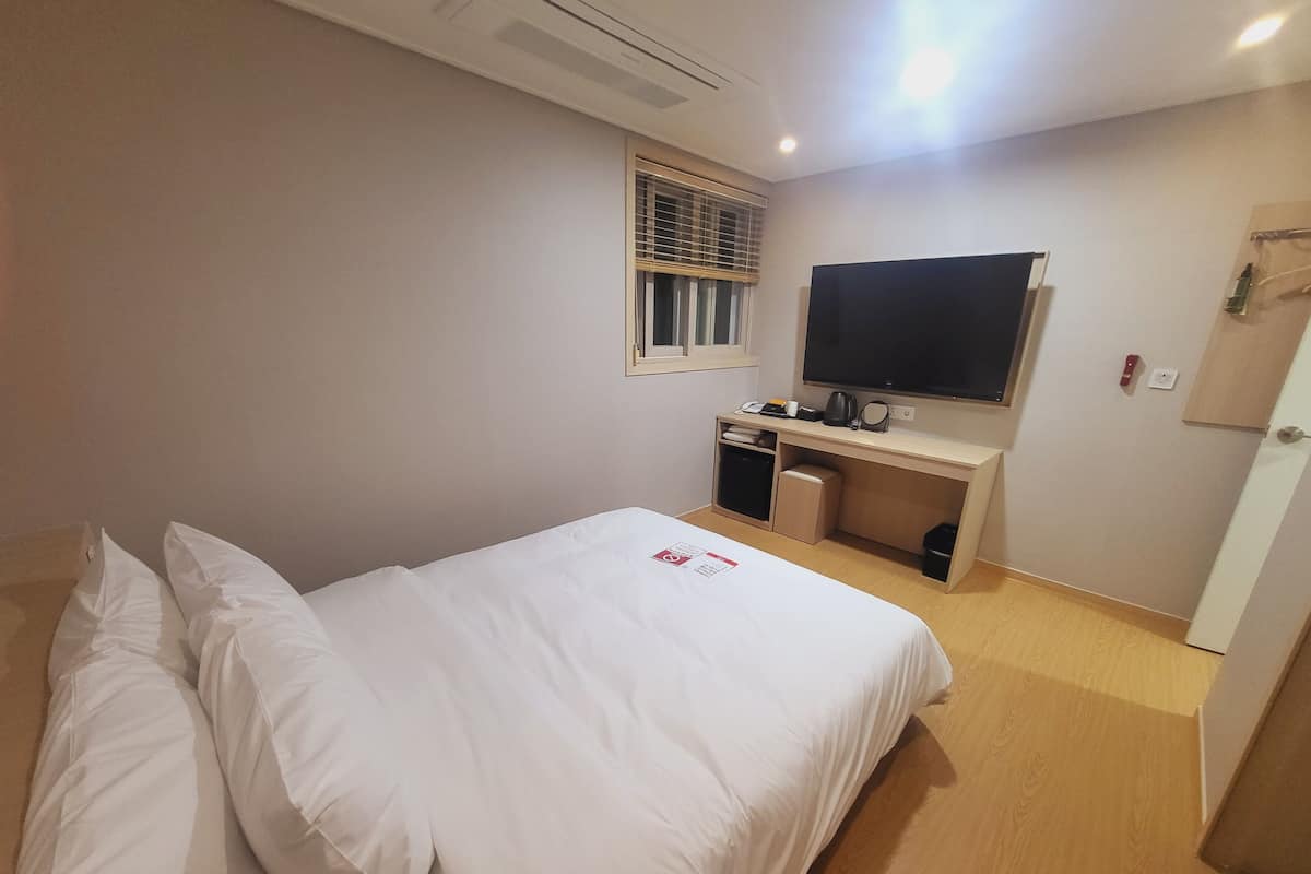 A hotel room with a bed, a desk, a television, and a window with blinds.