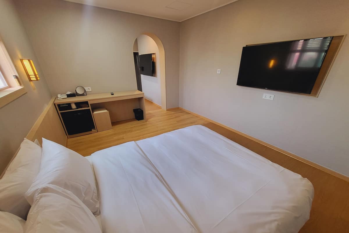 A hotel room with a bed, a desk, a chair, a TV, and a mirror.