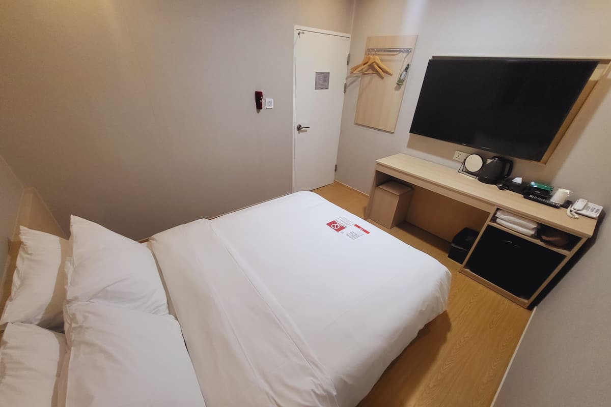 A hotel room with a bed, a desk, a television, and a coat rack.