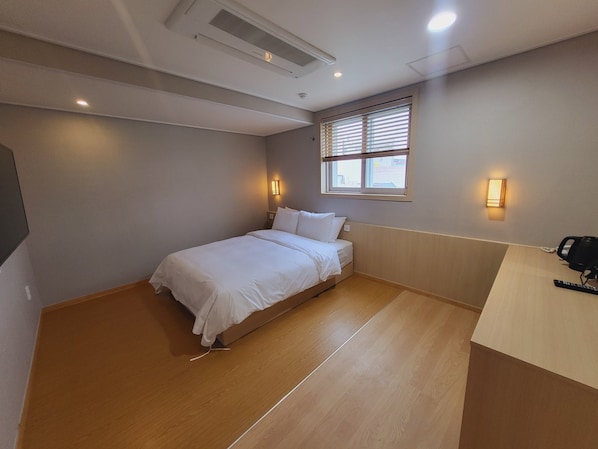 A bedroom with a bed, wooden flooring, a window with blinds, and wall-mounted lights. - Hotel Raza B (Pohang)