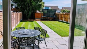 A patio with a round table and chairs, surrounded by a wooden fence and a grassy lawn. - Lovely 3-bed House in Lytham Saint Annes (Lytham St. Anne's)