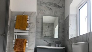 A modern bathroom with a marble wall, a toilet, a sink, and a towel rack with a yellow towel. - Lovely 3-bed House in Lytham Saint Annes (Lytham St. Anne's)