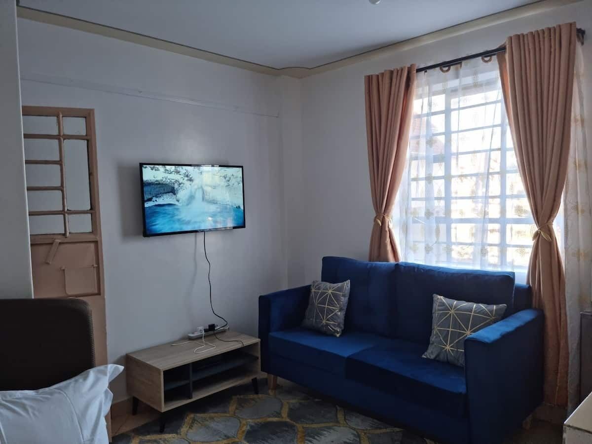Un soggiorno con un divano blu, una TV a parete e una finestra con tende.