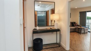 Een moderne hotelkamer met een grote spiegel, een console tafel met een lamp, een prullenbak en uitzicht op het buitengebied met zitplaatsen.
