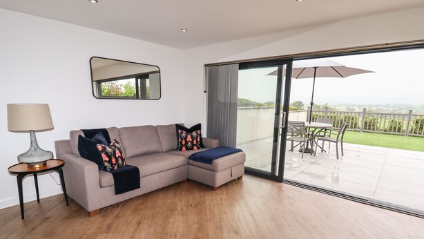 Een moderne woonkamer met een hoekbank, een bijzettafeltje en een grote glazen schuindeur die leidt naar een terras.