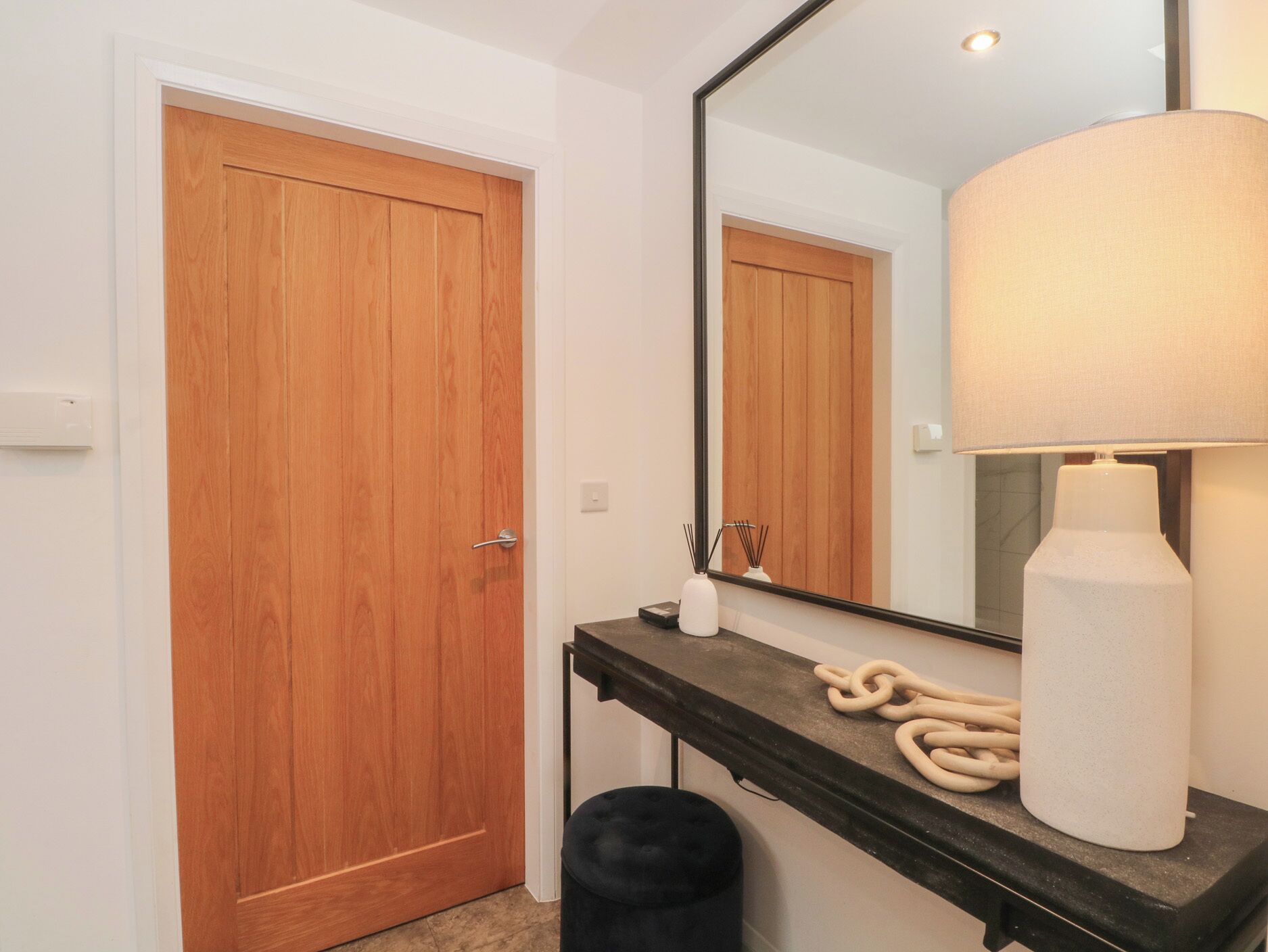 A bathroom with a wooden door, a mirror, a towel dispenser, and a black stool.