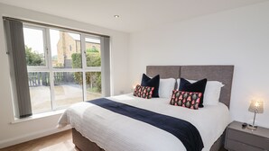 Een slaapkamer met een groot bed, een nachtkastje en een raam met gordijnen.