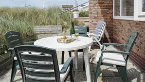 A round outdoor table with chairs, a bottle of wine, and glasses on a patio with a brick wall and vegetation in the background. - Lovely apartment in Bergen aan Zee (Bergen aan Zee)