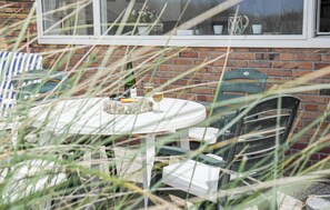 An outdoor patio with a round table, chairs, and a brick wall. - Lovely apartment in Bergen aan Zee (Bergen aan Zee)