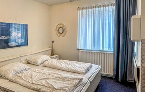 A bedroom with two beds, a radiator, a window with curtains, a wall-mounted mirror, and a framed picture. - Lovely apartment in Bergen aan Zee (Bergen aan Zee)