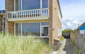 A two-story brick building with a balcony, a narrow pathway, and a wooden fence. - Lovely apartment in Bergen aan Zee (Bergen aan Zee)