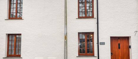 Un edificio blanco con puerta y ventanas de madera. Hay un banco frente al edificio.