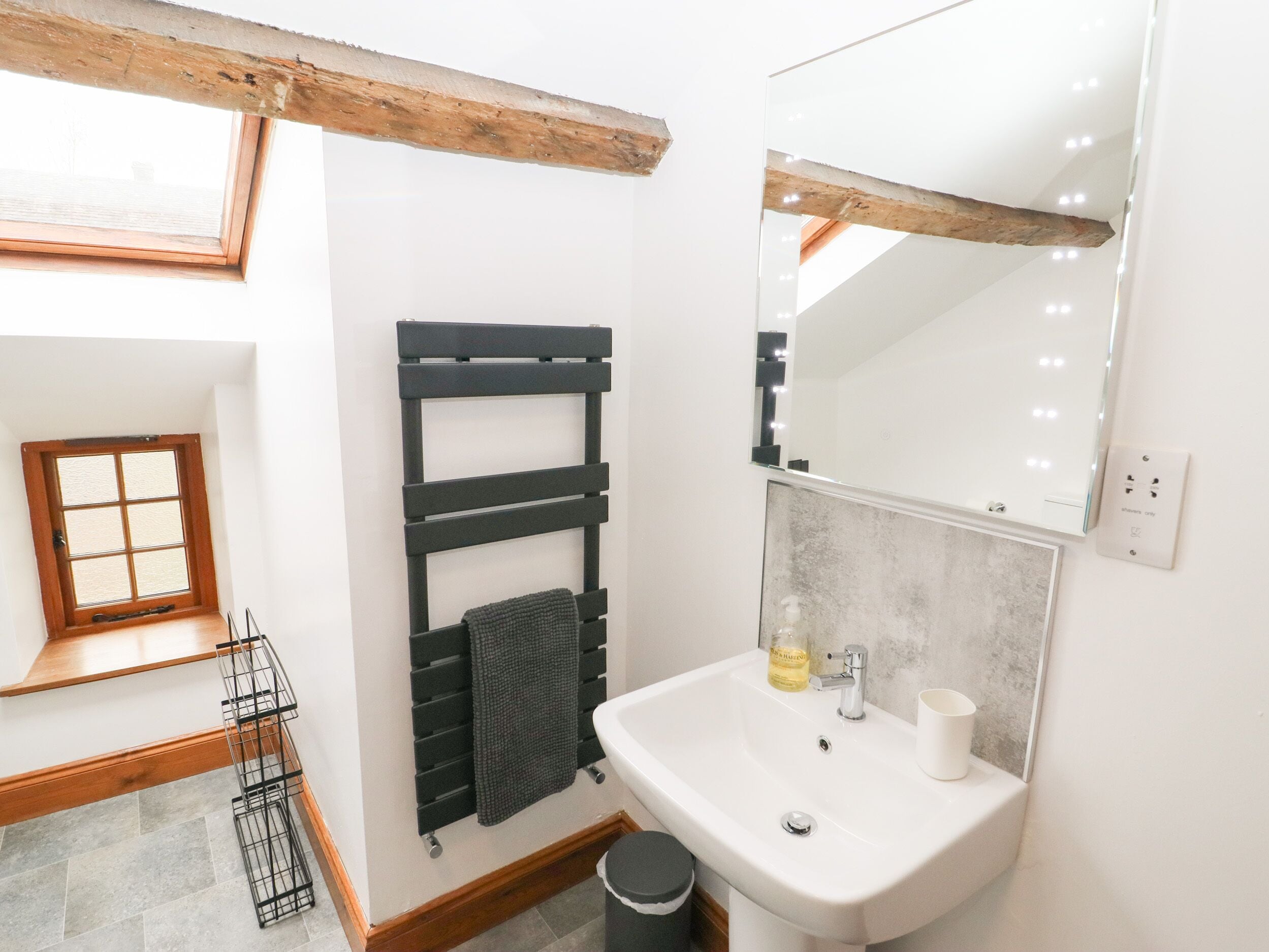 A bathroom with a white sink, a mirror, a towel rack, and a window with wooden beams.
